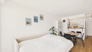 A modern bedroom with a large bed, a dining area with a table and chairs, and a kitchen in the background. - Sea view for 2, beach 100m away (Erquy)