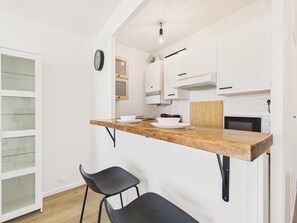 Une cuisine moderne avec des meubles blancs, un plan de travail en bois, une chaise noire et une horloge au mur.