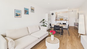 A modern living room with a sofa, dining table, chairs, and a small side table with a vase of flowers. - Sea view for 2, beach 100m away (Erquy)