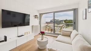 A modern living room with a flat-screen TV, a sofa, a round side table with a vase, and a balcony with chairs. - Sea view for 2, beach 100m away (Erquy)