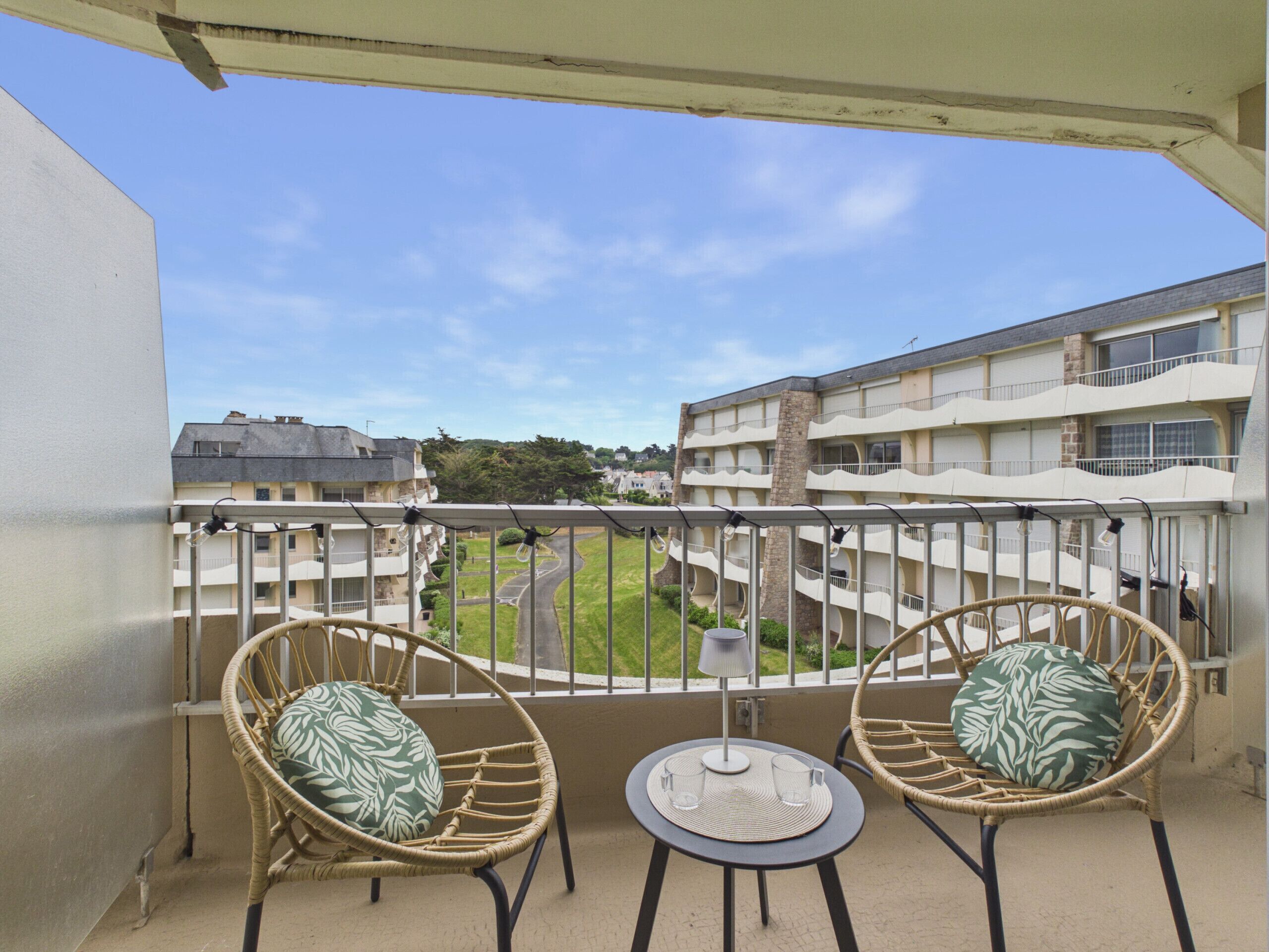 A balcony with two wicker chairs, a small round table, and a view of a residential area.