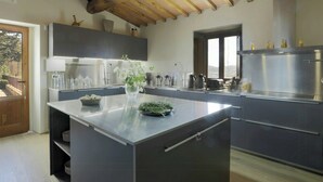 Een moderne keuken met een centraal kookeiland, roestvrijstalen apparatuur en houten balken in het plafond.