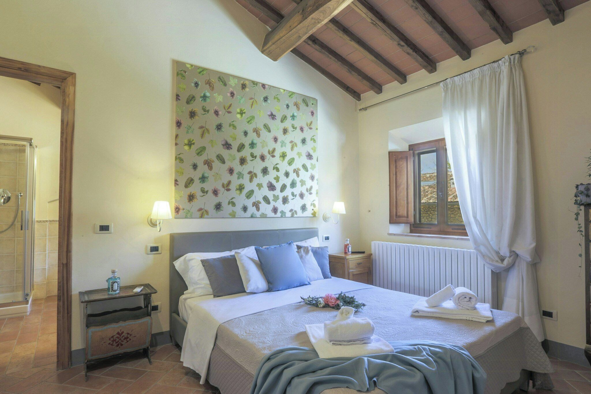 A bedroom with a bed, bedside tables, a shower, a window with curtains, and a wall with a floral pattern.