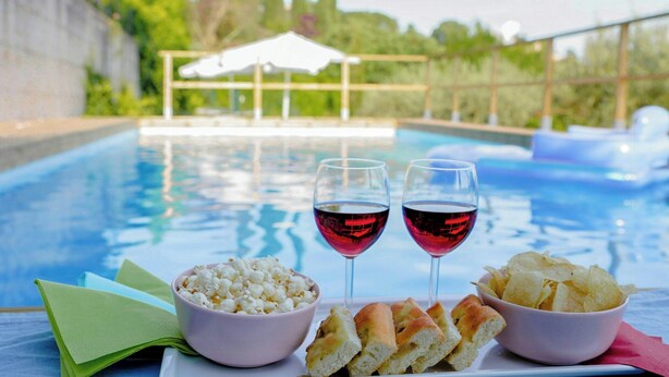 Een zwembadterras met een tafel, twee glazen rode wijn, schalen met popcorn en chips, en een servet.