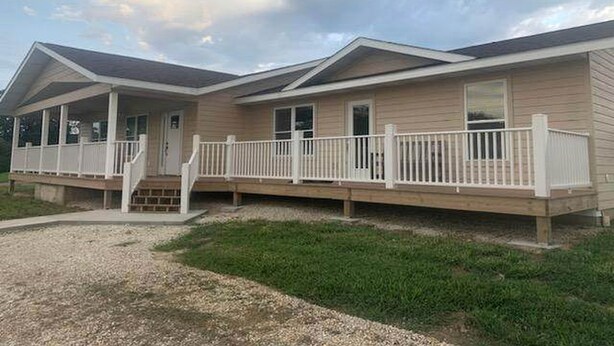 A two-story mobile home with a covered porch and a fenced deck.