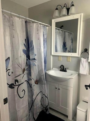 A bathroom with a shower curtain featuring a floral pattern, a white sink with a mirror above it, and a white toilet. - Charming Vacation Rental near Owensville, Missouri - Ideal for a Glamping Retreat with Family and Friends (Boulware Township)