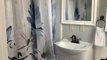 A bathroom with a shower curtain featuring a floral pattern, a white sink with a mirror above it, and a white toilet.