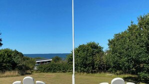 Twee witte Adirondack stoelen op een houten terras met uitzicht op de oceaan en een gebouw op de achtergrond.