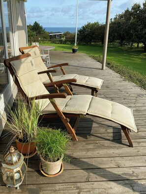 Una terraza de madera con sillones de descanso y plantas en macetas.