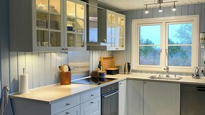 Een moderne keuken met witte kasten, een inbouwoven en een raam met uitzicht op bomen.