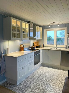 Una cocina moderna con armarios blancos, horno integrado y ventana con vistas a árboles.