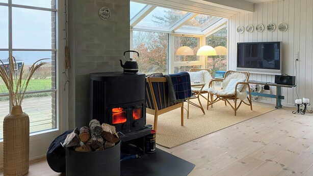 Een knusse woonkamer met een houtkachel, comfortabele zithoek, een televisie en een groot raam met uitzicht op de omgeving.