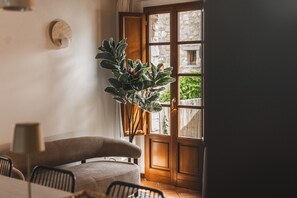 Ein Zimmer mit Holztür, einem Blumentopf, einem braunen Sofa und einem Esstisch mit Stühlen.