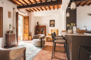 A spacious living area with a wooden ceiling, a kitchen with a bar, and a dining area with chairs and a rug. - Borgo di Gaiole – Stylish Tuscan Retreat with Pool in the Heart of Chiant (Gaiole in Chianti)