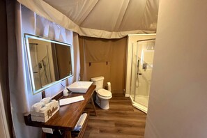 Un baño pequeño con tocador de madera, un espejo grande, un inodoro y una ducha con mampara de vidrio.