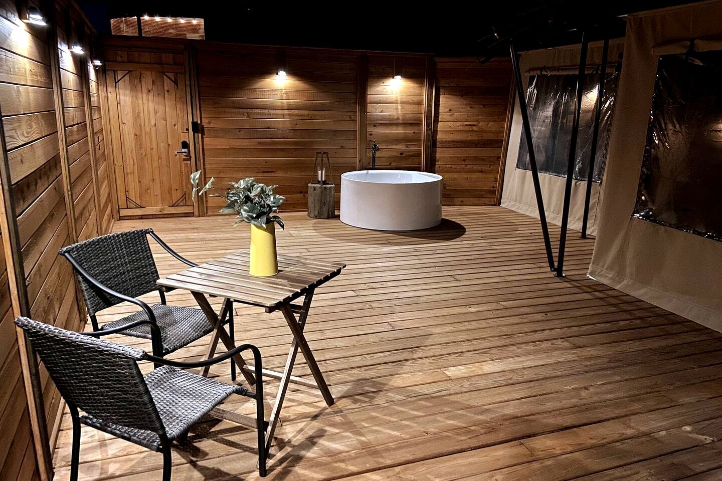 A wooden deck with a table and chairs, a potted plant, and a round seating area.