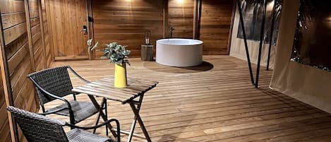 A wooden deck with a table and chairs, a potted plant, and a round seating area.