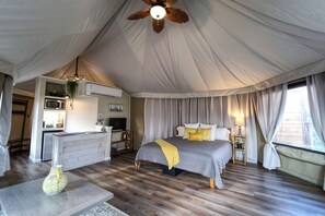Alojamiento en tienda de campaña con cama, mesita de noche, lámpara y zona de kitchenette.