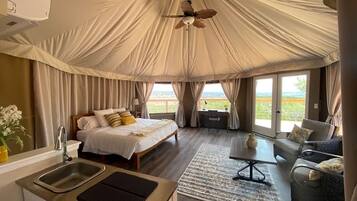 Una habitación tipo tienda de campaña con cama, escritorio, silla y vistas al exterior.
