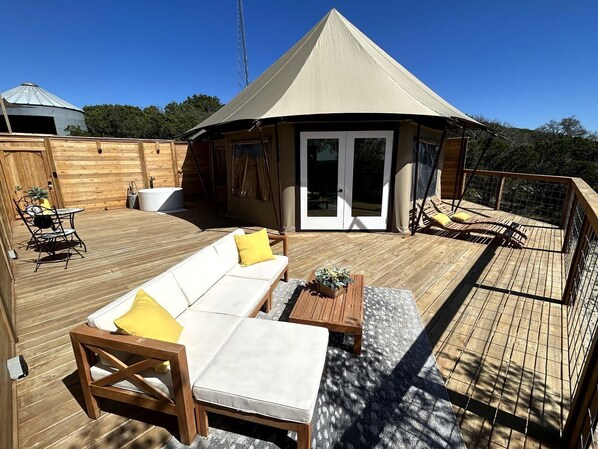 A covered outdoor area with a wooden deck, a white sofa with yellow cushions, and a wooden table.