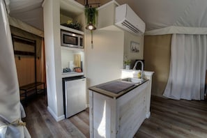 Eine kleine Küche mit Mikrowelle, Kühlschrank, Spüle und hängenden Pflanzen.