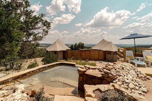 A hot tub area with two tents, a pool, and a wooden deck with lounge chairs.