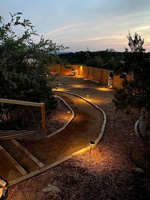 Ein angelegter Garten mit einem gewundenen Weg, Holzkonstruktionen und stimmungsvoller Beleuchtung.