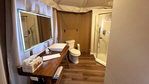 Ein kleines Badezimmer mit einem Holzbadschränkchen, einem großen Spiegel, einer Toilette und einer Duschkabine.