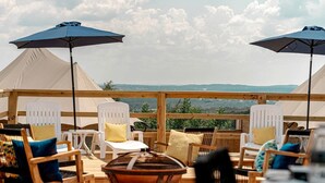 Eine Dachterrasse mit weißen Stühlen und Tischen, zwei großen Sonnenschirmen und Blick auf die Landschaft.