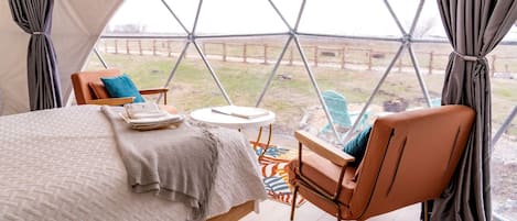 Un ambiente acogedor con una cama, una silla, una mesita y vistas a través de un ventanal.