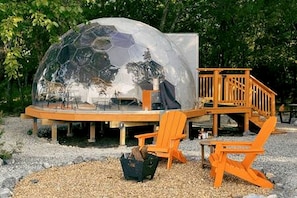 Une structure en forme de dôme géodésique dotée d’une terrasse en bois, d’un espace salon extérieur et d’une petite table.