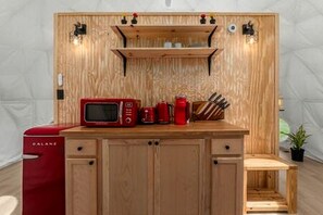 Une petite cuisine équipée d’un four à micro-ondes, d’une machine à café et d’ustensiles de cuisine, le tout installé sur un plan de travail en bois.