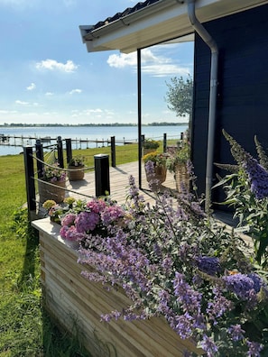 Une terrasse en bois avec vue sur un lac, une zone délimitée par une clôture et des plantes en pot.
