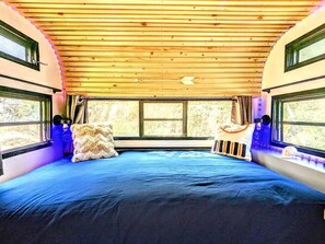 Un interior acogedor con una cama, almohadas y una ventana que da a zonas verdes.
