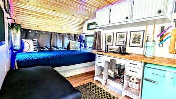 A compact RV interior with a bed, kitchenette, and storage cabinets.