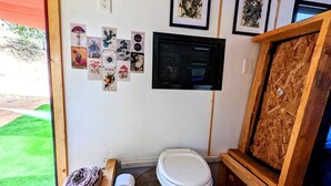 A compact bathroom with a toilet, a small trash bin, and a framed picture collection on the wall. - Sunshine Retreat- VCT#2 Glamping in Santa Ysabel, CA (Santa Ysabel)