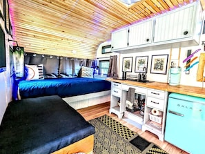 Interior de una caravana compacta con cama, kitchenette y armarios de almacenamiento.
