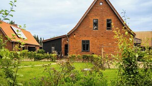 A brick house with a triangular roof, a front door, and a small garden with plants and a bench. - Idyllic country house between Hamburg and Berlin (Langen Jarchow)