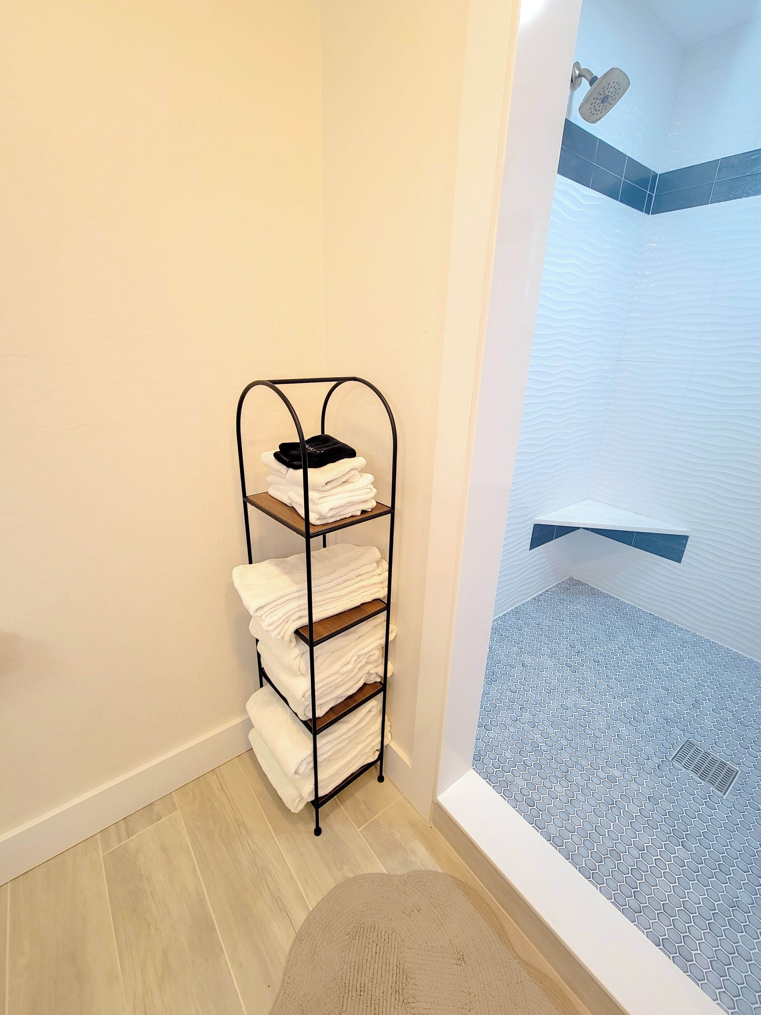 Une salle de bain avec une douche, une étagère en métal où sont pliées des serviettes, et un sol à motifs hexagonaux.
