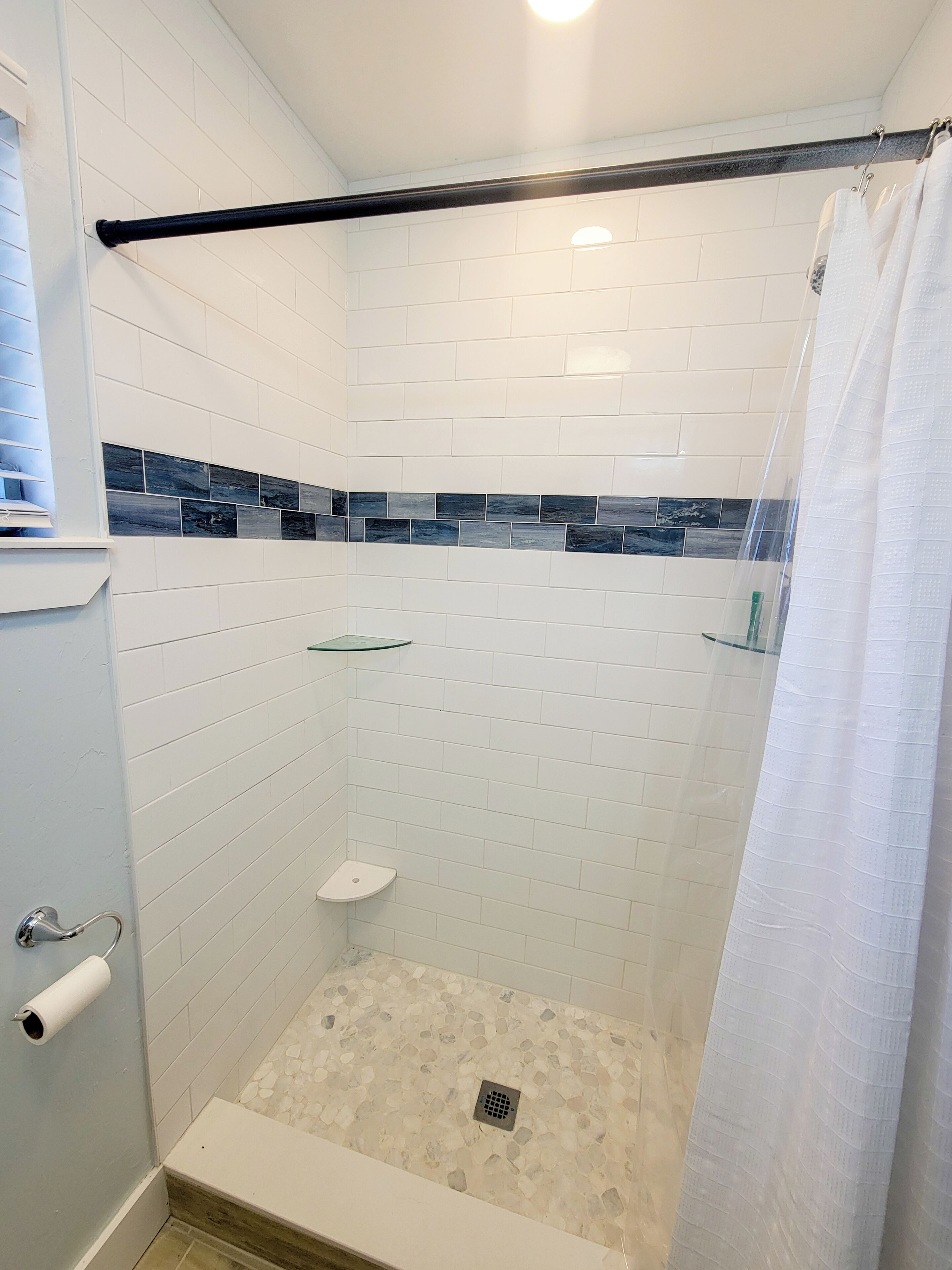 A shower area with white tiled walls, a glass shelf, a white toilet, and a shower curtain.