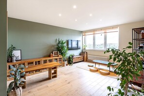 A spacious room with a wooden bench, a television, and a large window with a city view. - Design-led Flat Near Notting Hill (London)
