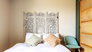 A bed with white bedding and two pillows, a teal chair, and a decorative headboard. - Design-led Flat Near Notting Hill (London)