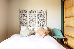 Ein Bett mit weißer Bettwäsche und zwei Kissen, ein türkisfarbener Sessel und ein dekorativer Kopfseitenverzierer.
