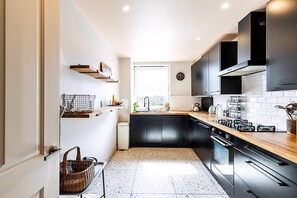 A modern kitchen with black cabinets, a wooden countertop, and a window providing natural light. - Design-led Flat Near Notting Hill (London)