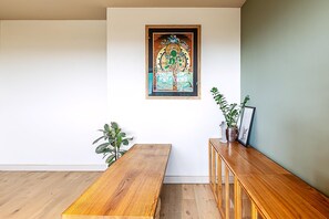 Ein Zimmer mit einer hölzernen Sitzbank, einem kleinen Tisch, einer Kommode mit Dekoration und einem gerahmten Bild an der Wand.