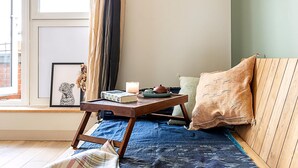 A cozy room with a wooden bench, a small table with a book and candle, a framed picture, and a window with curtains. - Design-led Flat Near Notting Hill (London)