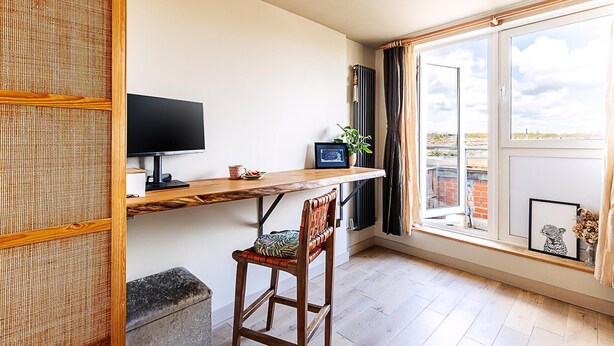A room with a wooden desk, a television, a window with curtains, a potted plant, and a framed picture. - Design-led Flat Near Notting Hill (London)