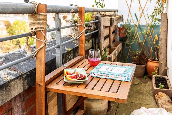 Een houten tafel met een boek, een glas en een fruitschaal op een balkon.