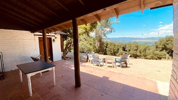 Un área de patio techada con mesa y sillas, un muro de ladrillo y vistas del paisaje.