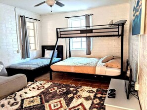 A room with a bunk bed, a sofa, a patterned rug, and a ceiling fan.